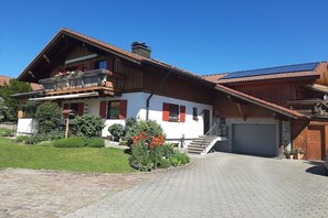 Eine zweistöckige Chalet mit einem geneigten Dach, einem Balkon mit Blumenkästen und einer gepflasterten Auffahrt.