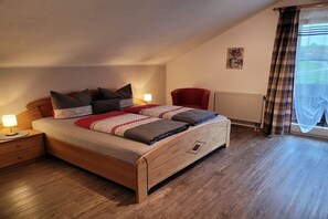 A bedroom with a wooden bed, a nightstand, a red chair, a radiator, and a window with curtains. - Holiday apartment with 2 bedrooms (Hopferau)