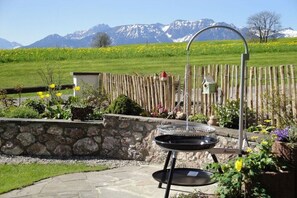 Eine Terrasse mit einer Steinmauer, einem Metallgrill und einem Holzzaun.