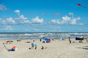 Una playa con gente, tiendas de campaña y una cometa roja.