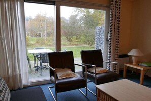 Una habitación con dos sillones de cuero, una mesa de madera, una lámpara y vistas al exterior con coches y vegetación.