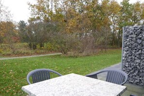Un área de estar al aire libre con una mesa y sillas, rodeada por un muro de piedra y árboles.