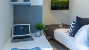 Quarto moderno com uma cama, uma escrivaninha com um laptop, uma TV na parede e uma pequena planta na escrivaninha.