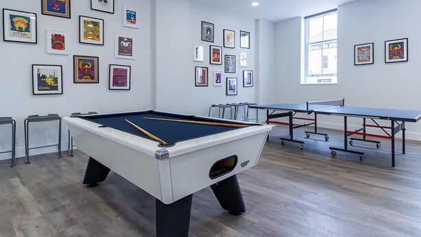 A pool table in a room with a modern design, featuring artwork on the walls and a large window providing natural light.