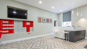 Um espaço de escritório moderno com uma televisão de tela plana grande, um armário de arquivo vermelho, um balcão de recepção e um piso com padrão geométrico em Chevron.