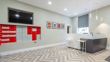 Un espacio de oficina moderno con una gran televisión de pantalla plana, un archivador rojo, un mostrador de recepción y un suelo con estampado de tablero de ajedrez.