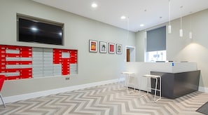 A modern office space with a large flat-screen TV, a red filing cabinet, a reception desk, and a chevron-patterned floor. - AXO  - Seven Sisters - London (London)