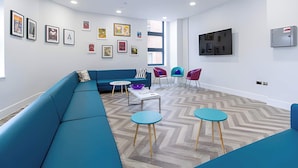Uma área de estar moderna com um sofá azul, duas mesas redondas e cadeiras coloridas.