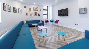 A modern lounge area with a blue sofa, two round tables, and colorful chairs. - AXO  - Seven Sisters - London (London)