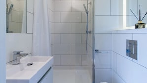 Uma casa de banho moderna com chuveiro, pia e espelho.