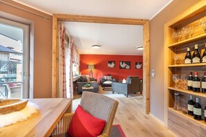 A modern living room with a red accent wall, a dining area with a wooden table, and a wine rack with bottles and glasses. - Holiday apartment with 2 bedrooms (Oberstdorf)