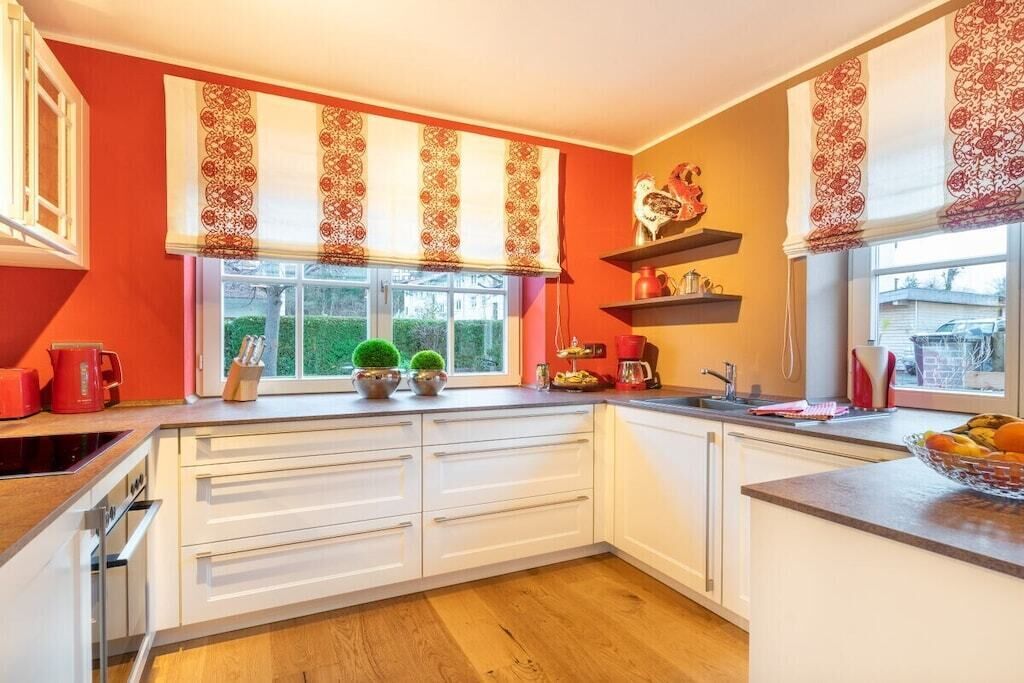 A modern kitchen with white cabinetry, a window with decorative valance, and a countertop with kitchenware.
