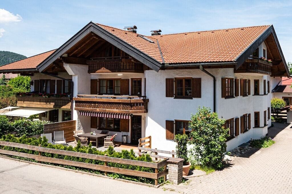 A two-story chalet with a balcony, wooden shutters, and a paved driveway.