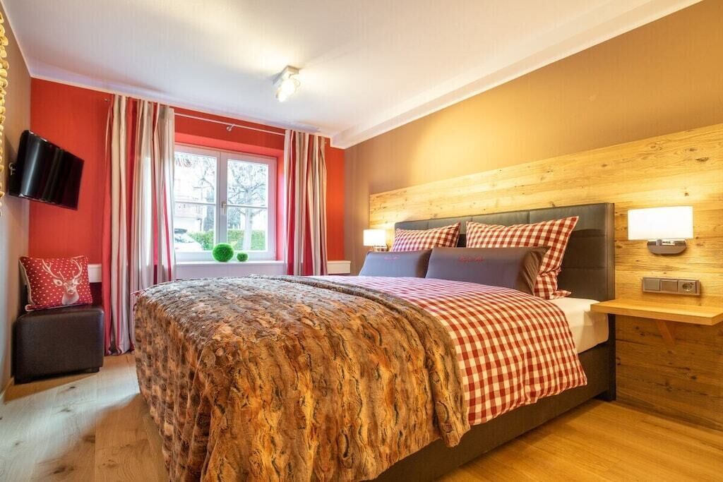 Un dormitorio con una cama grande, cabecera de madera, televisor en la pared y ventana con cortinas.