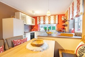 A kitchen with a dining area, white cabinets, and a window with patterned curtains. - Holiday apartment with 2 bedrooms (Oberstdorf)
