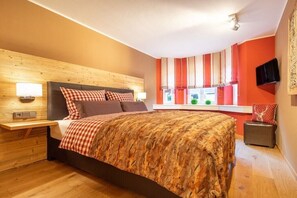 A bedroom with a bed, bedside tables, a window with curtains, and a mounted television. - Holiday apartment with 2 bedrooms (Oberstdorf)