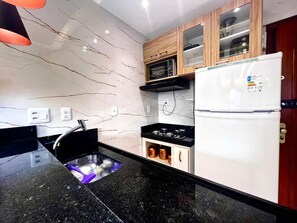 A kitchen with a black countertop, a built-in microwave, a white refrigerator, and a wooden cabinet with jars. - 1904 Nazaré Apto 2 quartos com Garagem (Belém)