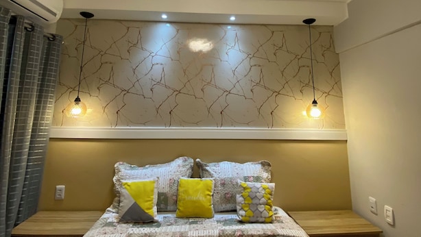 A bedroom with a bed, bedside tables, a wall-mounted air conditioner, and a ceiling light fixture. - 1904 Nazaré Apto 2 quartos com Garagem (Belém)