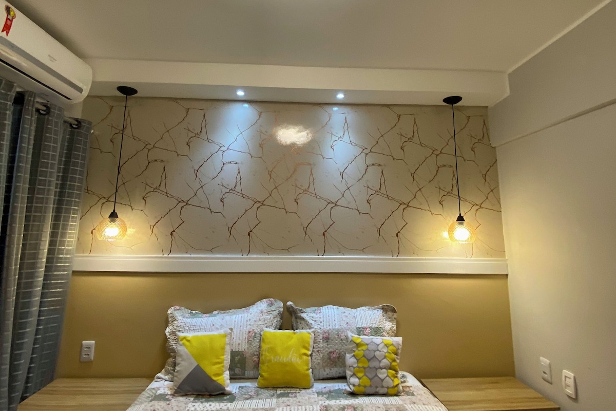 Un dormitorio con cama, mesitas de noche, aire acondicionado instalado en la pared y una lámpara en el techo.