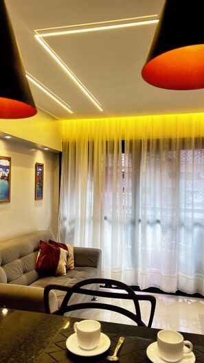 A modern living room with a sofa, a dining table with two cups, and a window with sheer curtains. - 1904 Nazaré Apto 2 quartos com Garagem (Belém)