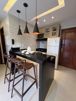 Una cocina moderna con una isla central, taburetes de bar, iluminación colgante y electrodomésticos integrados.