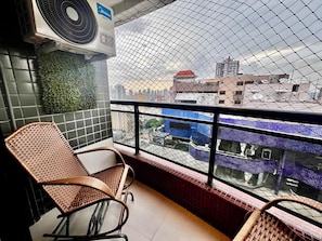 A balcony with a view of the city, a wicker chair, and an air conditioning unit. - 1904 Nazaré Apto 2 quartos com Garagem (Belém)