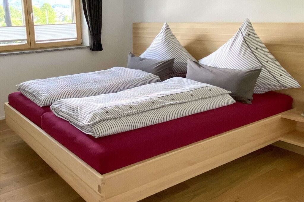 A single bed with a wooden frame, a red mattress, and striped bedding.