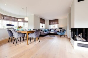 Ein modernes Wohnzimmer mit Essbereich, Kamin und großen Fenstern.
