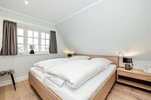 Ein Schlafzimmer mit einem Bett, Nachttischlampen, einem Fenster mit Vorhängen und einem Sessel.