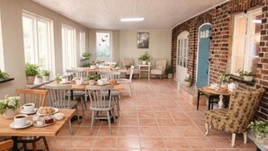 A cozy cafe with multiple tables and chairs, a brick wall, and a blue door labeled 'B&B'. - Tunnby Gårdshotell (Nyhamnsläge)