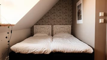 Een slaapkamer met een schuine plafond, een bed met hoofdeinde en een aan de muur hangend schilderij.