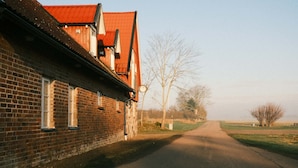 A narrow road leading to a brick building with a red roof, surrounded by open fields and leafless trees. - Tunnby Gårdshotell (Nyhamnsläge)