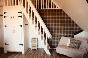 Quarto com escada de madeira, guarda-roupa branco, sofá branco e parede com padrão xadrez.