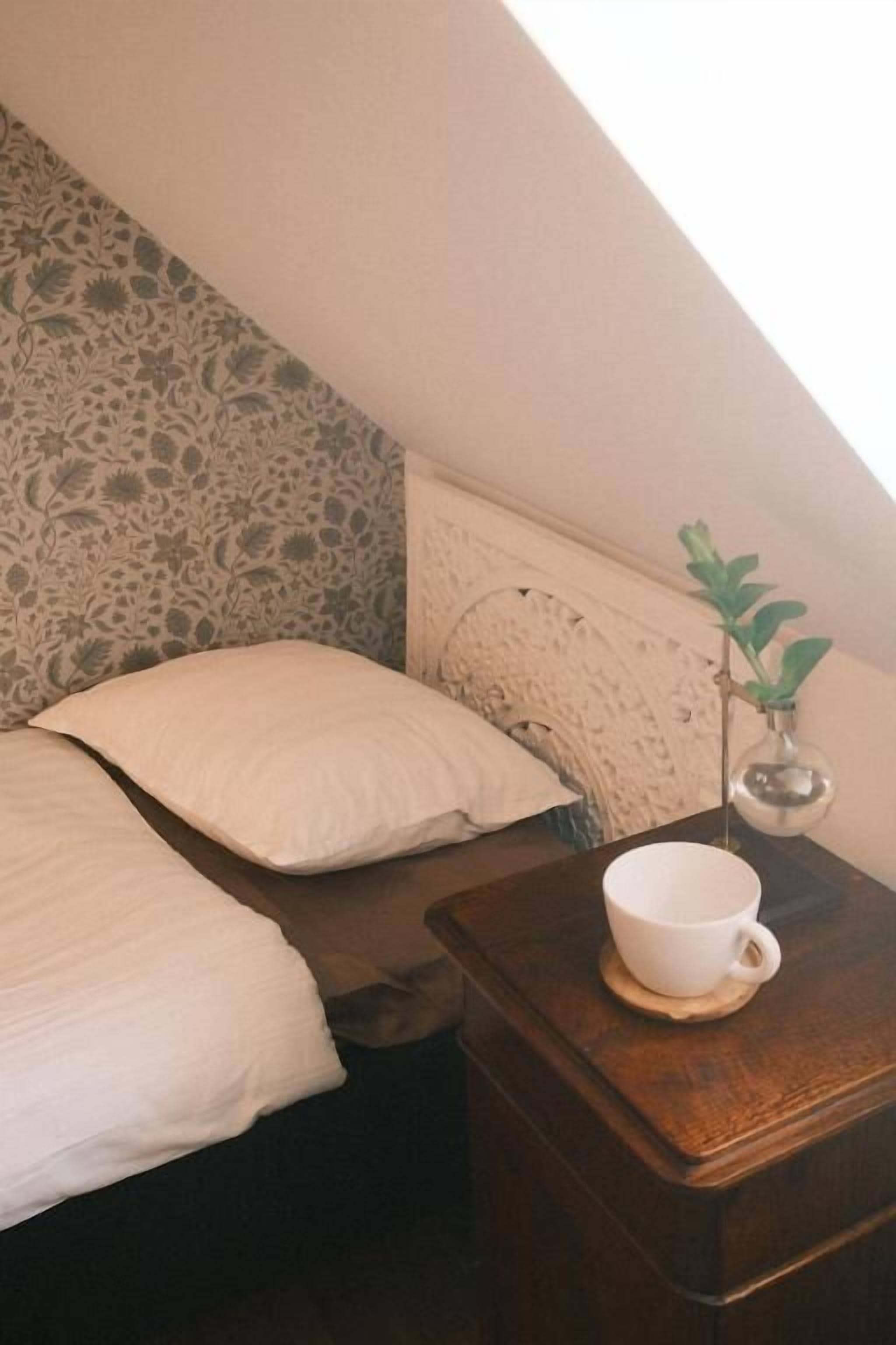 Een slaapkamer met een bed, een nachtkastje met een kopje en een plant.
