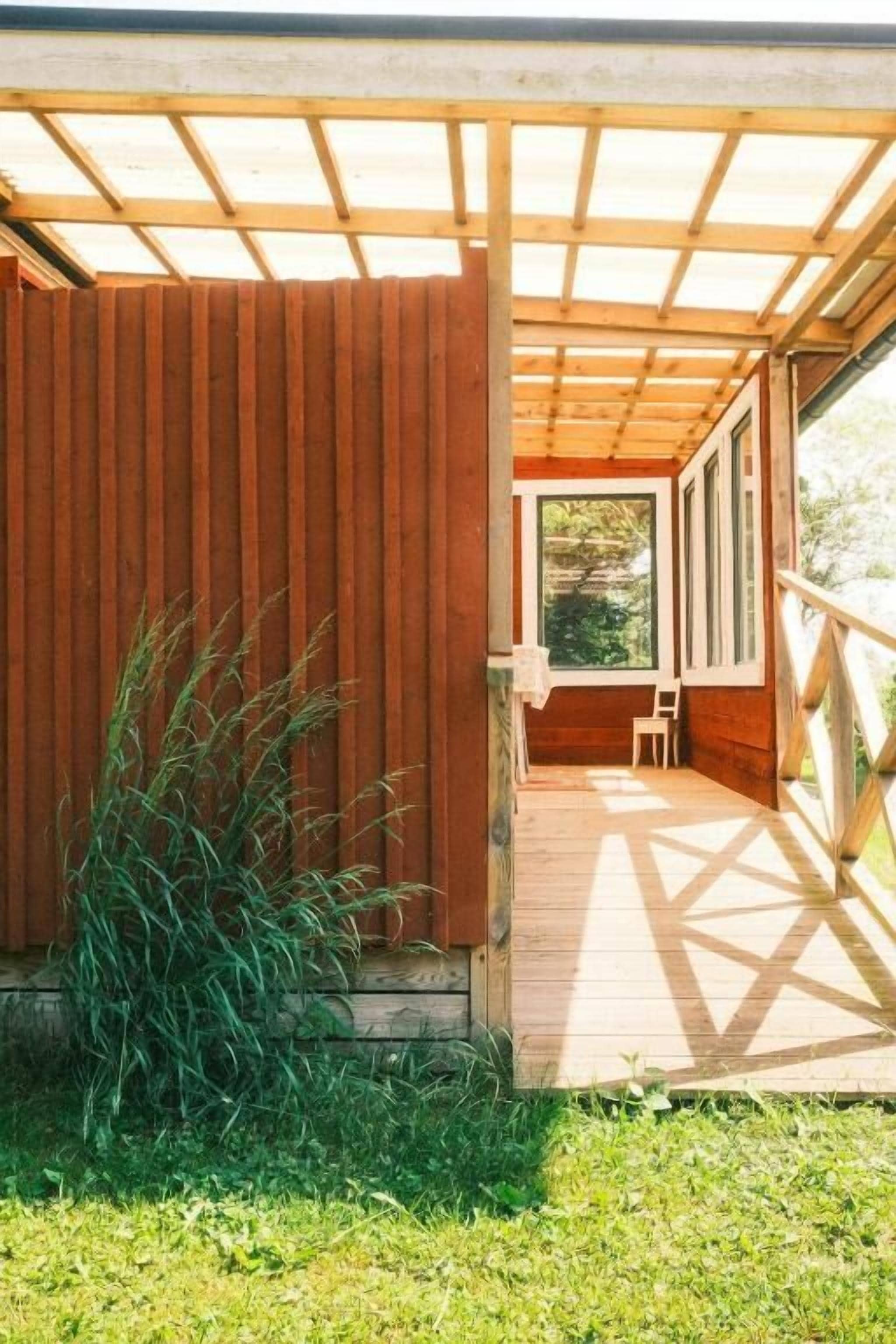 Un terrazzo in legno con una zona coperta, una sedia e vista su del verde.