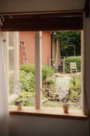 A window view of a garden with a ladder, chairs, and a small table.