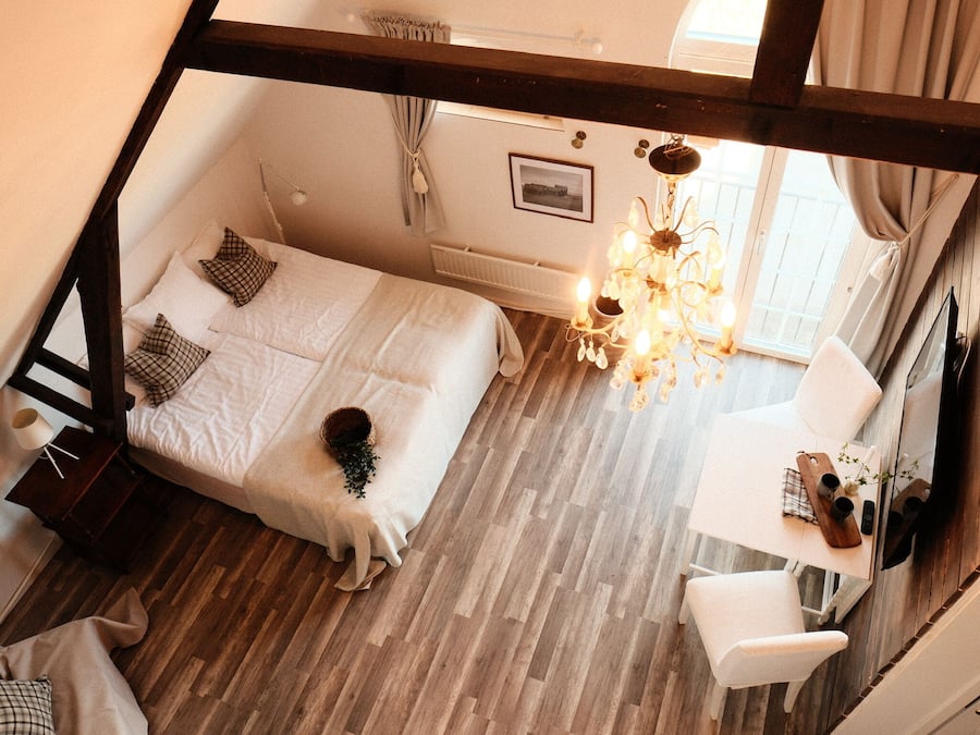 A bedroom with a bed, a chair, a desk, a chandelier, and a window.