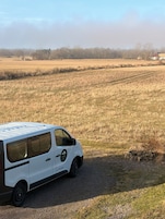 Una camioneta blanca estacionada en un camino de grava en un campo rural, con un granero al fondo.