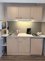 Cocina compacta equipada con microondas, lavamanos y cafetera.
