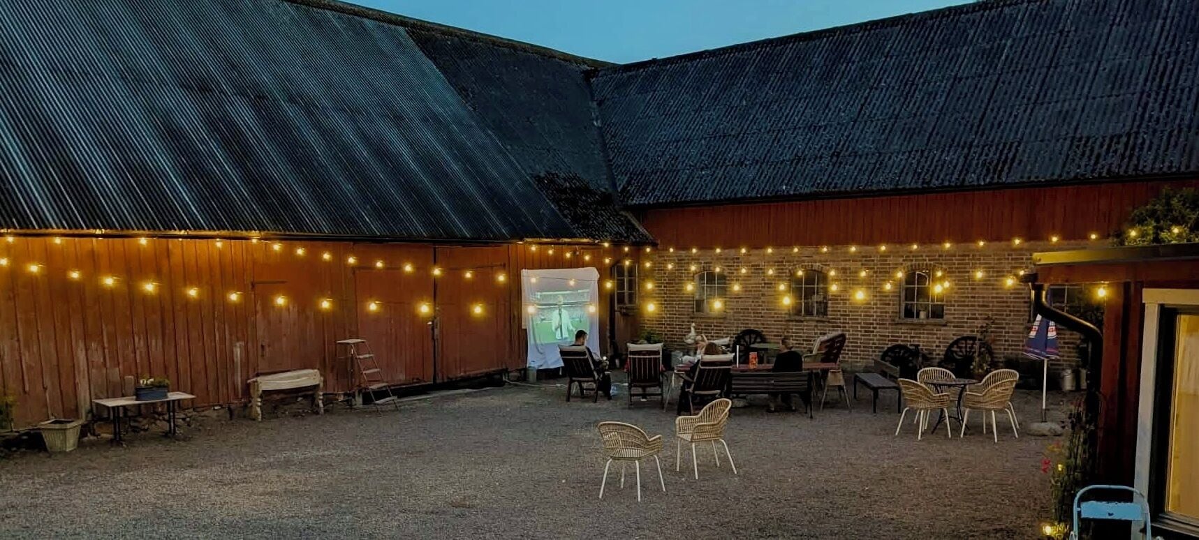 An outdoor seating area with tables and chairs, string lights, and a barn-like structure.
