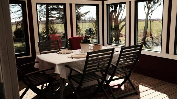 A covered dining area with a table set for four, surrounded by chairs, and large windows offering a view of the outdoors. - Tunnby Gårdshotell (Nyhamnsläge)
