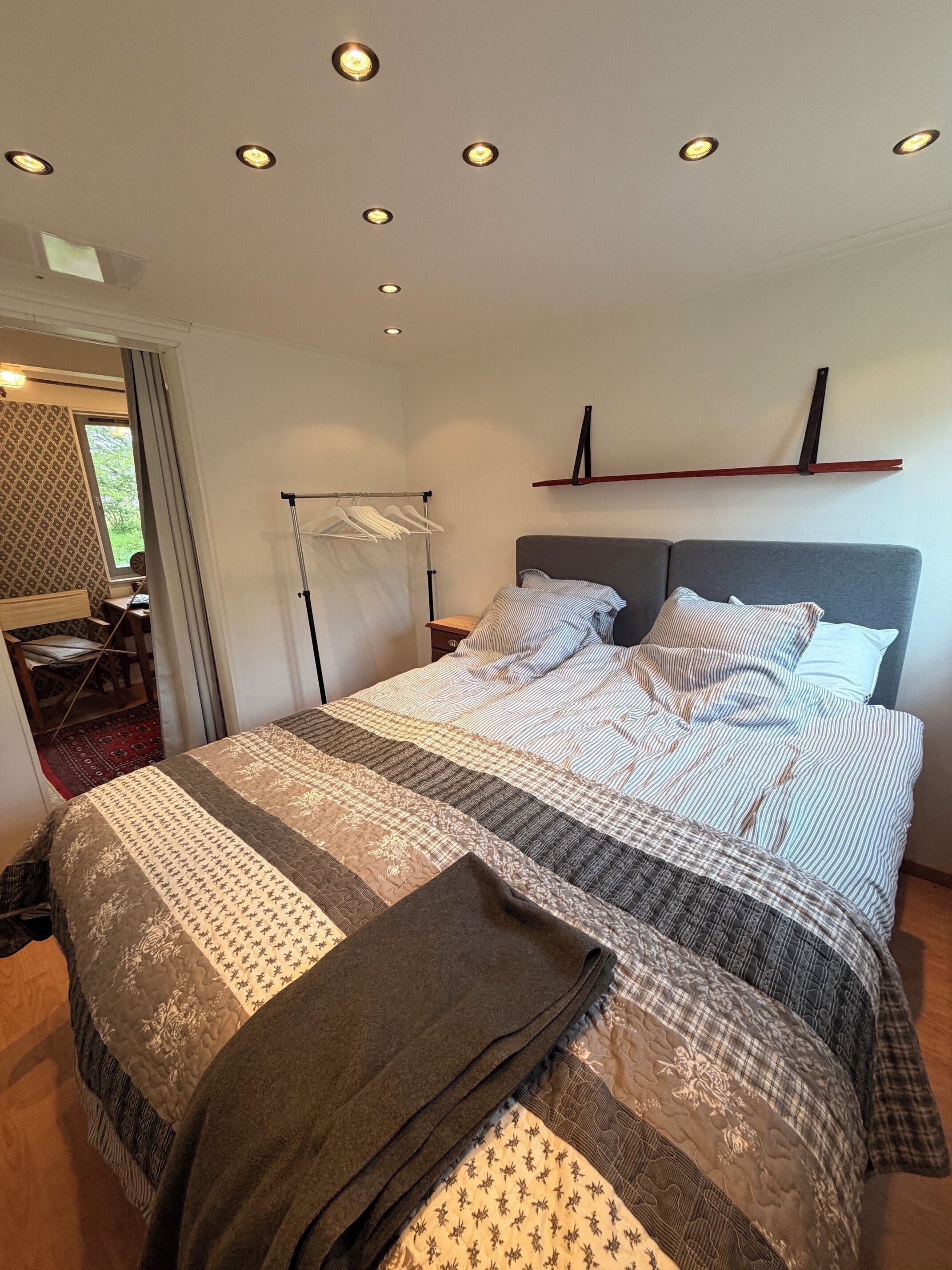 Quarto com cama grande, mesa de cabeceira, luminária pendente e janela com cortinas.