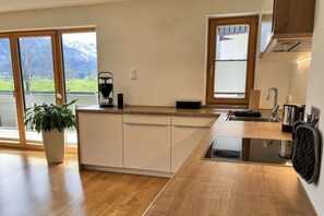Une cuisine moderne dotée d’un plan de travail en bois, d’une cuisinière encastrée et d’une grande fenêtre offrant une vue sur les montagnes.