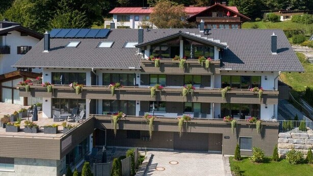 Een meerlaags gebouw met een plat dak, balkons met beplanting en een geplaveid pad.