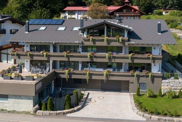 A multi-story building with a flat roof, balconies with plants, and a paved driveway. - Holiday apartment with 2 bedrooms (Oberstdorf)