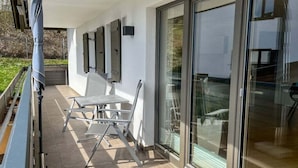 Een terras buiten met een tafel, stoelen, een overdekt gedeelte en een glazen deur naar een binnenruimte.