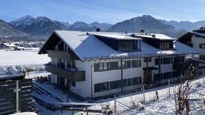 Een modern gebouw met een plat dak en grote ramen, omgeven door een met sneeuw bedekte omgeving en bergen op de achtergrond.