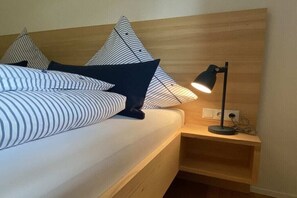 A neatly made bed with striped bedding and dark pillows, a bedside table with a lamp, and a wooden headboard. - Holiday apartment with 2 bedrooms (Oberstdorf)