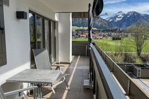 A balcony with a table and chairs, a view of a mountain range, and a small village in the distance. - Holiday apartment with 2 bedrooms (Oberstdorf)