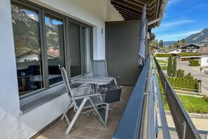 Un balcon avec une table et des chaises, une vue sur les montagnes et un ciel dégagé.